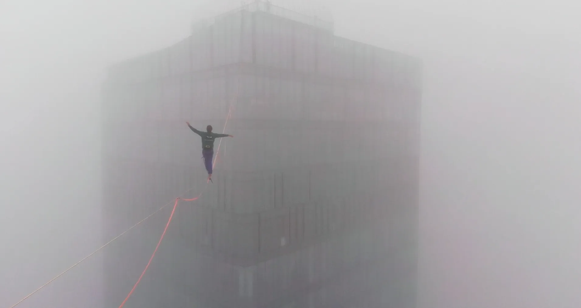A highliner walking a line between towers in fog.
