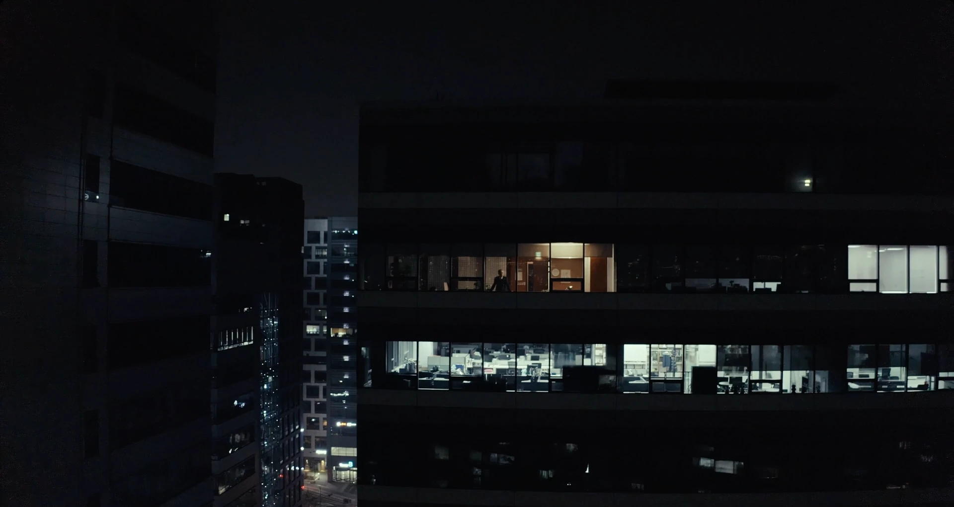 Illuminated offices seen through a building facade at night.