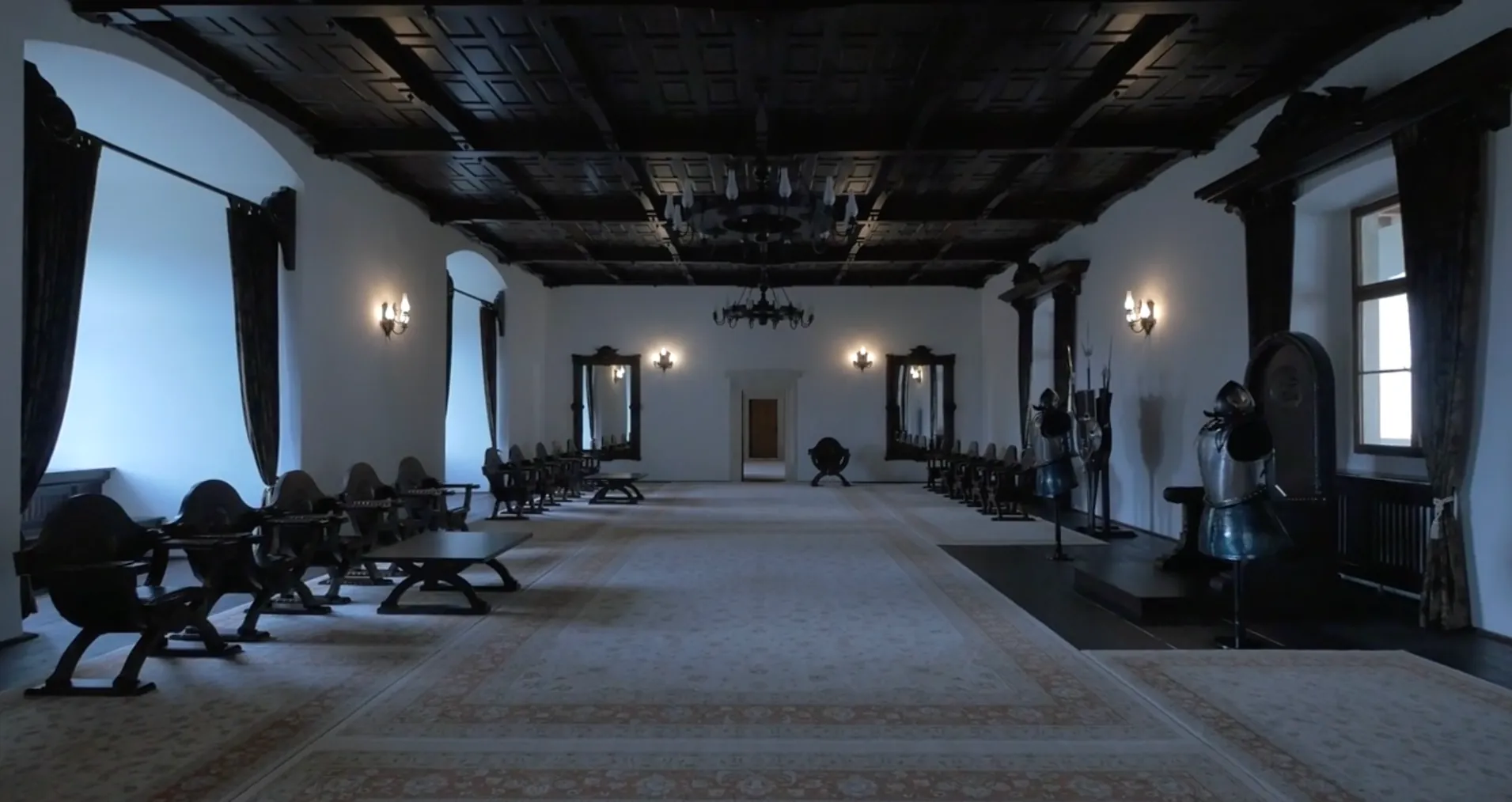 A panelled castle hall with carved chairs and suits of armour.